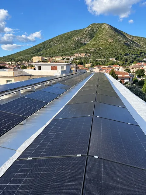 Pannelli fotovoltaici su un tetto piano, con la montagna e il paese sullo sfondo