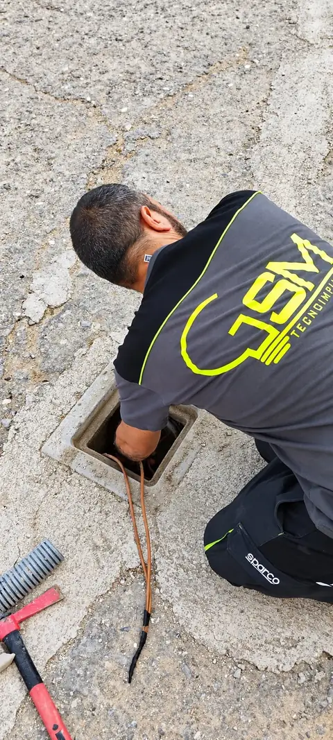 Un tecnico in polo G.S.M., inginocchiato, al lavoro sui cavi di un pozzetto a terra